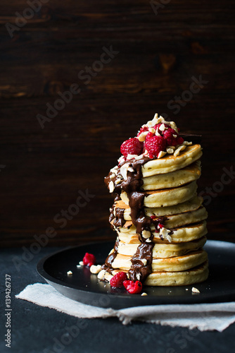 Stack of pancakes with a chocolate sauce and berries on dark background