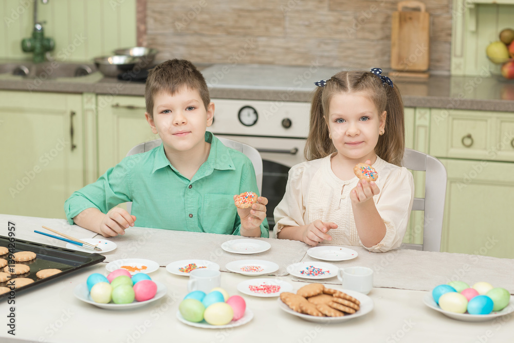 Fototapeta premium Cute children decorate cookies at a table in the home kitchen
