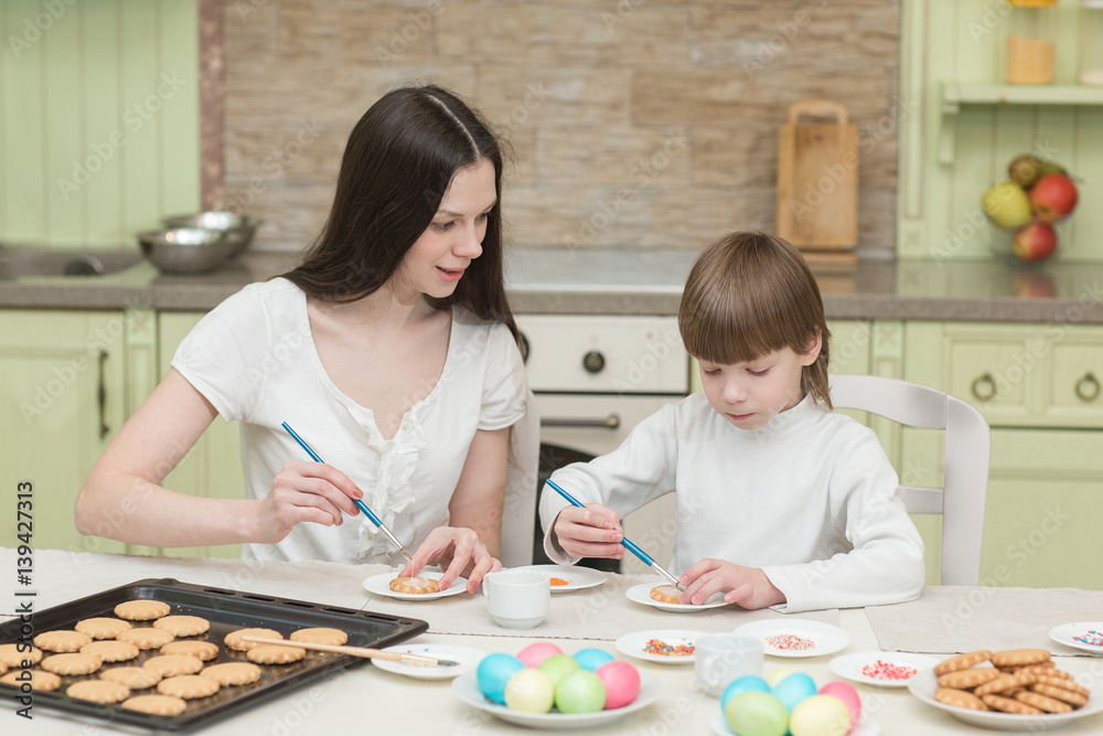 Young mum and her little son baking together and decorating the cupcakes