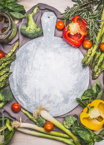 Asparagus and various vegetables around cutting board, top view, frame