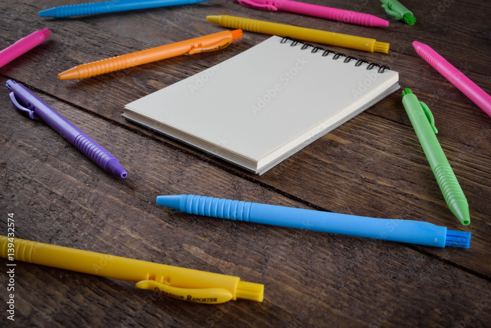colored pens with a notebook on a wooden background place for text