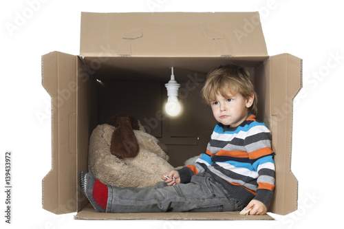 Billede på lærred Cute Toddler Boy with his Stuffed Toy in Cardboard Box with Bare Light Bulb, rep