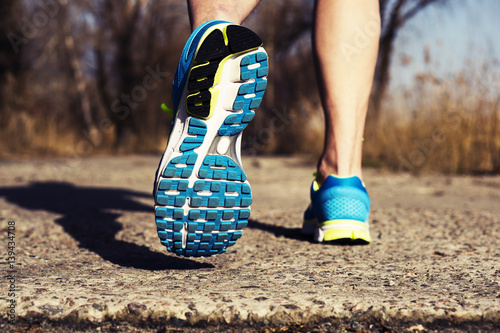 Back view of male muscular feet in sneakers walking on sidewalk in spring sunny day