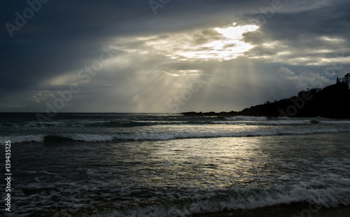 Sunlight bursting through clouds at dawn on tranquil beach