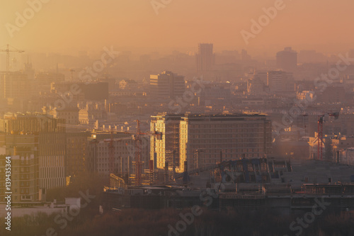 Close-up shooting from top of morning metropolitan city: huge stadium under construction with cranes and beams, residential buildings and districts, multiple facades, hazy horizon, Moscow, Russia