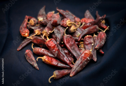 Dried red hot chili peppers are lying in a heap, glitering with different shades of red