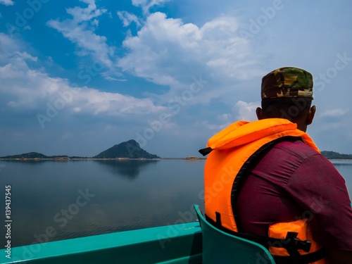 Man wearing orange color life jacket traveling in a boat taking a boat ride tour in a lake river in a national park in sri lanka