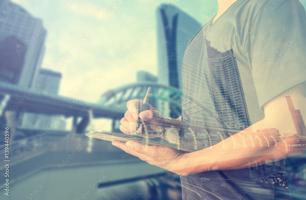 Double exposure of businessman using digital tablet with city landscape blurred background.