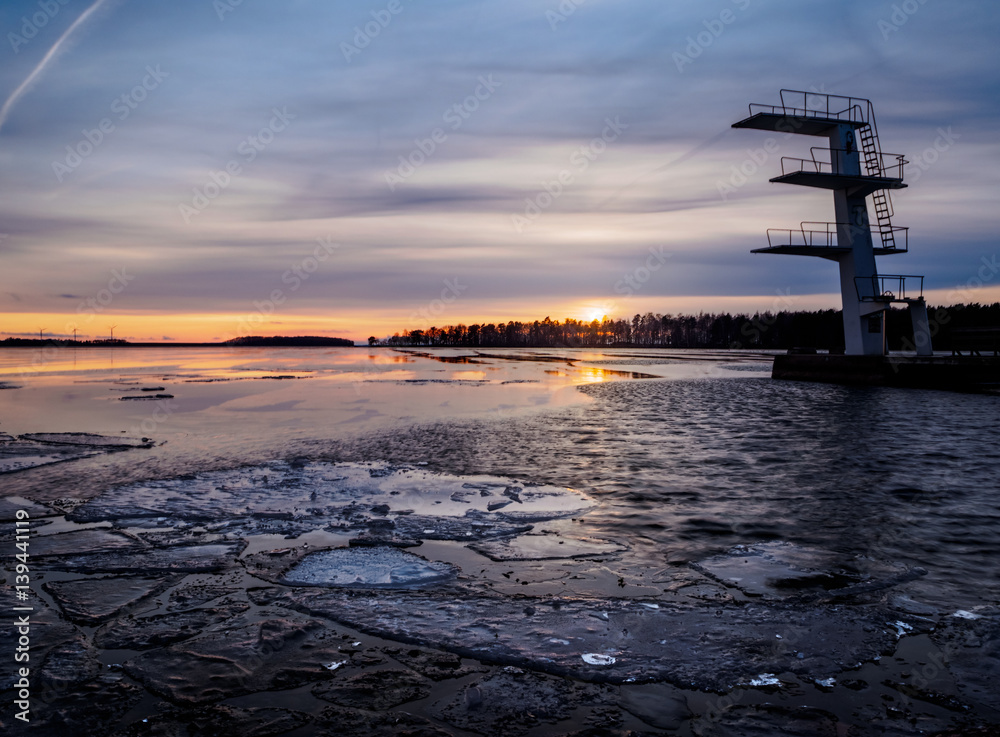 Diving tower at sunset in winter with ice on lake