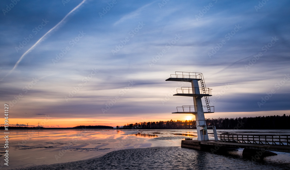 Diving tower at sunset in winter with ice on lake
