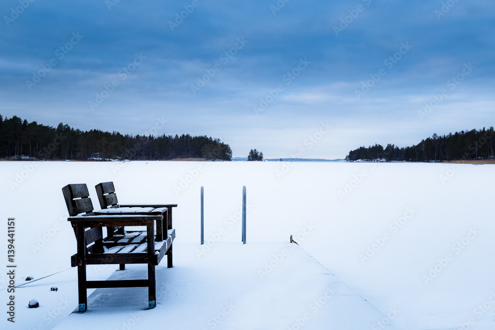 Bench on jetty at frozen lake with much snow