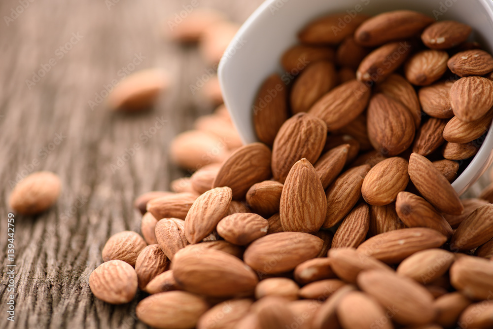almonds in a white ceramic bowl on grained wood background