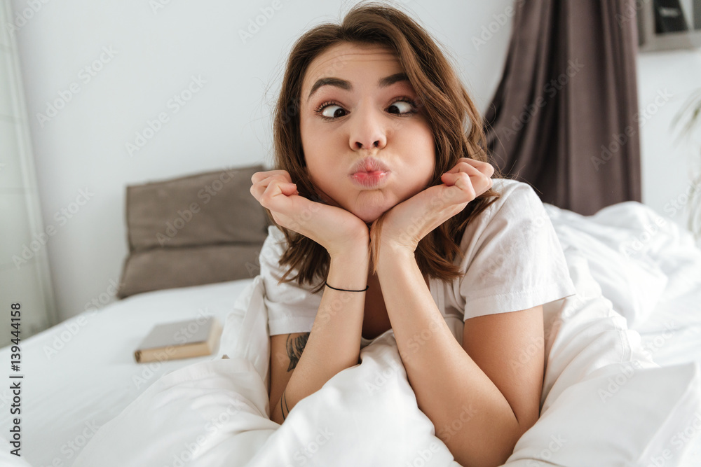 Amusing comical young woman making funny face lying in bed Amusing comical young woman making funny face lying in bed