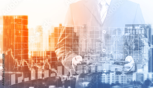 Double exposure of success businessman using digital tablet with city landscape background and forex graph.