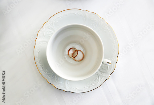 Два золотых кольца на в белой чашке и белом блюдце


