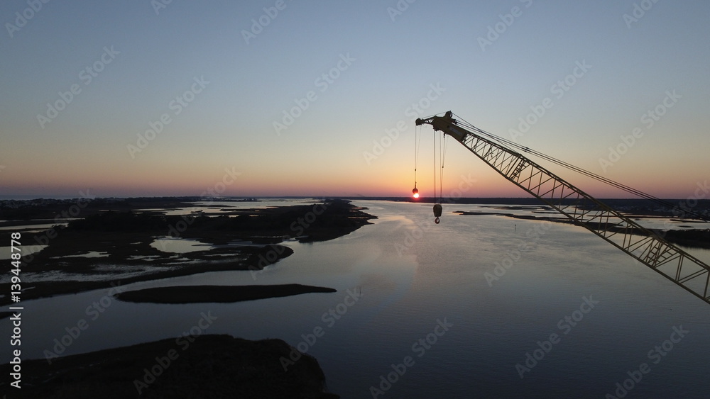 Aerial photo of a construction crane appearing to hoist the sun over the horizon. Aerial photo of a construction crane appearing to hoist the sun over the horizon.
