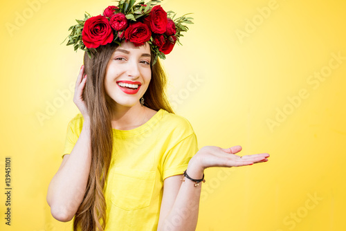 Colorful portrait of a beautiful woman in yellow t-shirt with wreath made of red roses on the yellow background