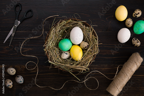 Easter eggs in nest, scissors and thread on a black background