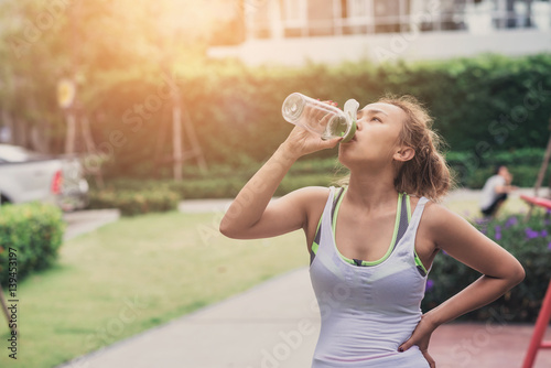 Beautiful Asian Sport Woman are Drinking Water After Running on Sunset Evening Summer Time