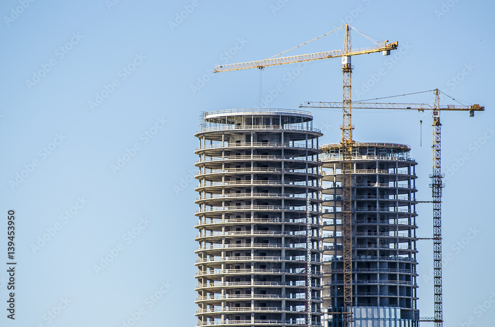 New buildings being constructed. Industrial building site. Shot of two lifting cranes and skyscrapers under construction on clear blue sky background. High-rise buildings and workers. Twin towers.