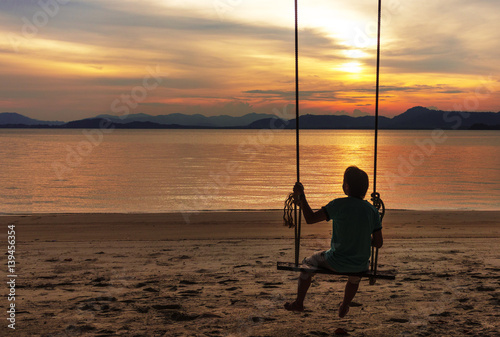 A man relaxing on wooden swing chair looking sunset on beach