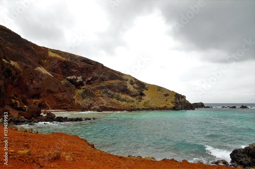 Long shot of the Ovahe beach, a small cove surrounded by red cliffs in Easter Island, Rapa Nui, Chile, South America photo