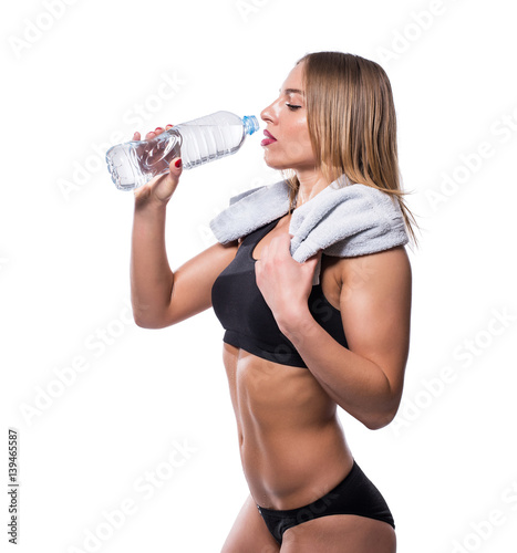 Attractive sexy woman after workout with towel and shaker isolated over white background. Healthy girl drinks pure water.