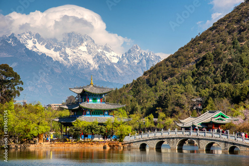 Amazing view of the Jade Dragon Snow Mountain and the Black Dragon Pool  Lijiang  Yunnan province  China. The Suocui Bridge over pond and the Moon Embracing Pavilion in the Jade Spring Park.