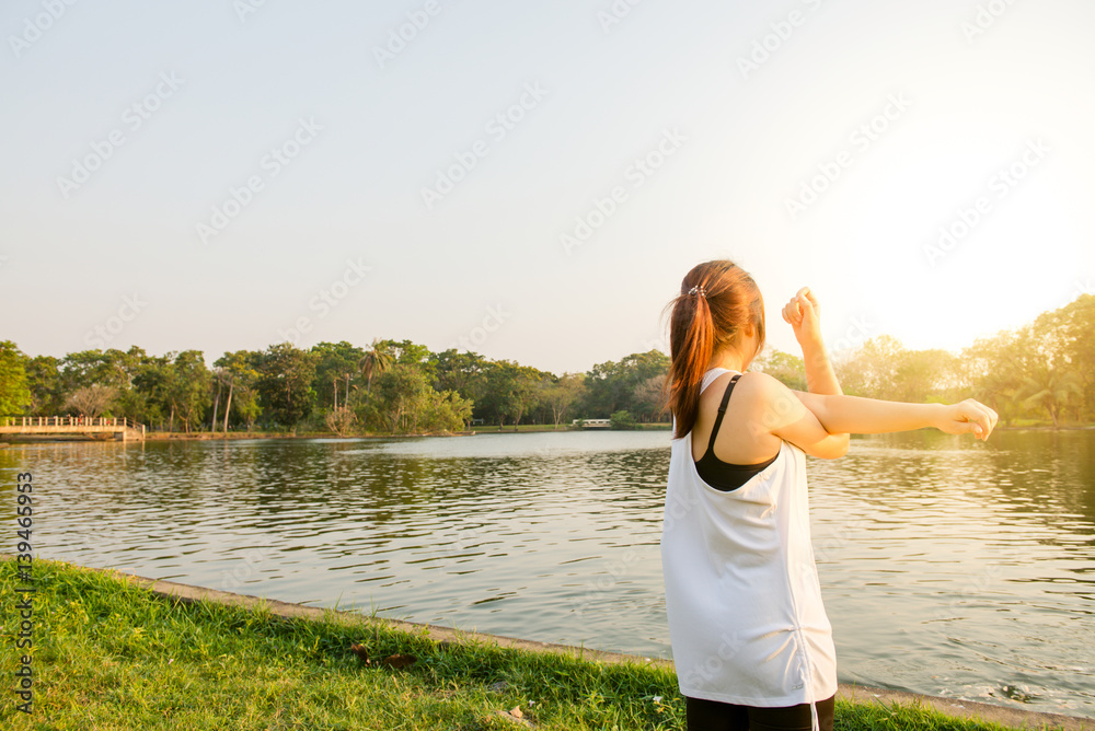 Happy successful sportswoman raising arms to the sky on golden back lighting sunset summer. Fitness athlete with arms up celebrating goals after sport exercising and working out outdoors. Copy space.