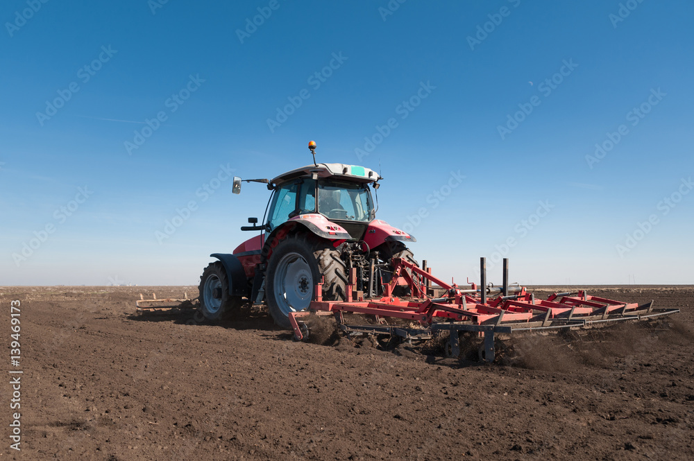 Naklejka premium Farmer in tractor preparing land with seedbed cultivator in early spring