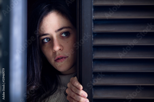 Worried Woman Watching Outside from a Wooden Window Shutter