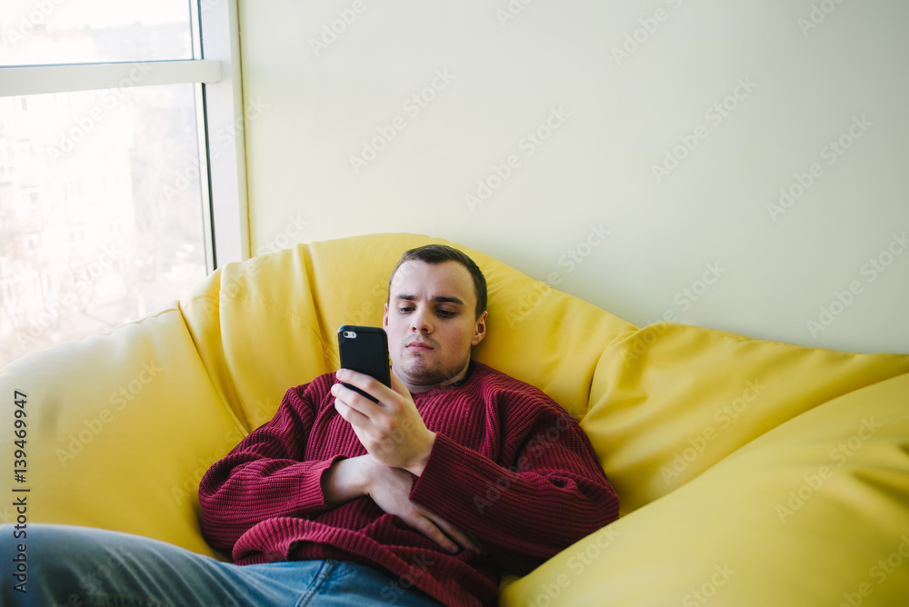 Obraz premium The young man is an office worker in a yellow armchair bag and use a smartphone. Break work.