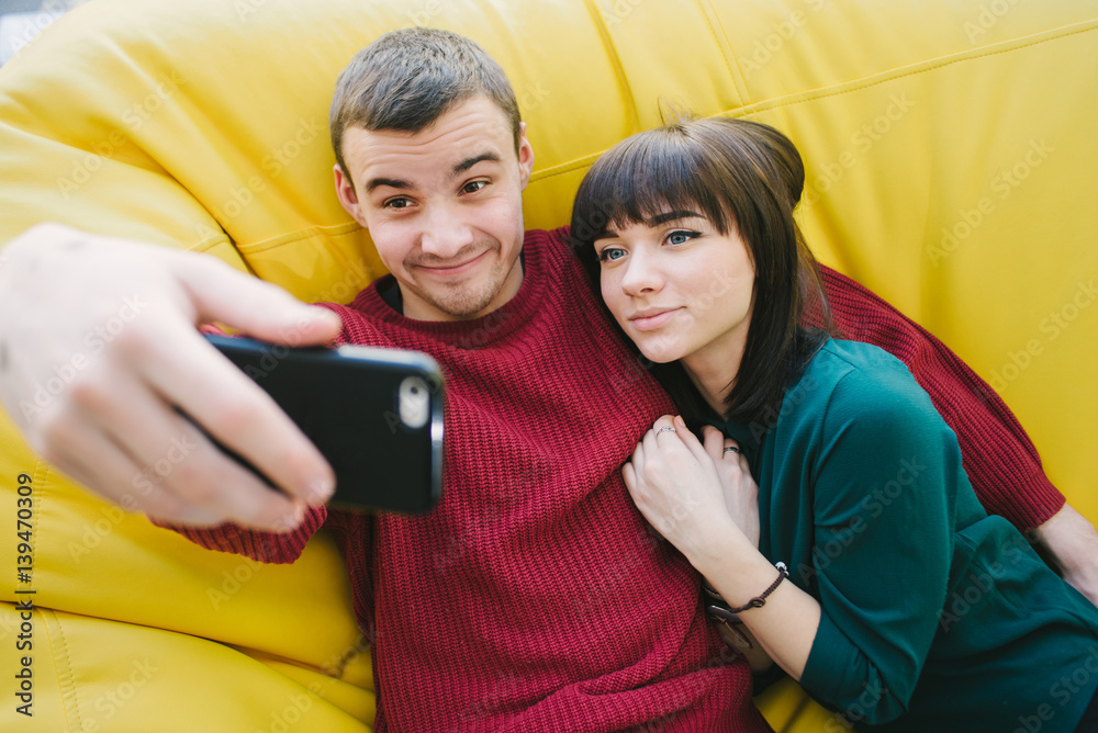Fototapeta premium A young couple in love hipster fun doing selfie on your smartphone. Portrait of young people in the room.