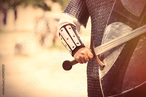 strong knight hand with beautiful sword and shield on the middle ages decoration background