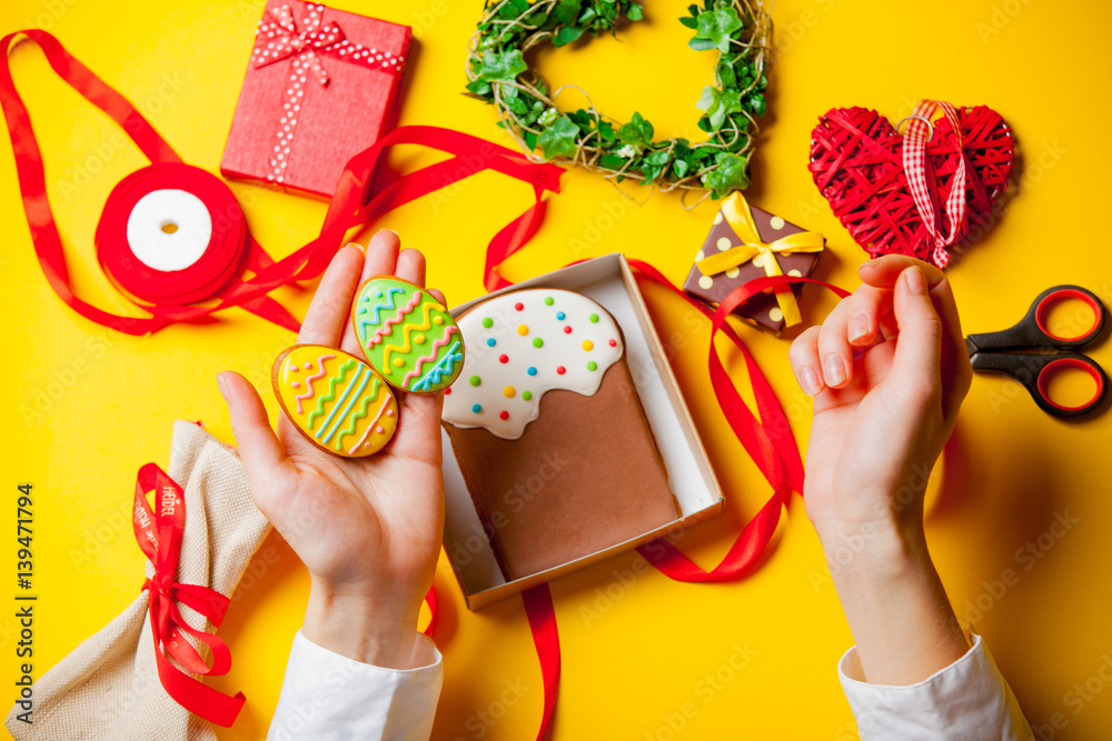 Fototapeta premium white caucasian female hands holding egg shaped cookie near things for decoration on the wonderful yellow background