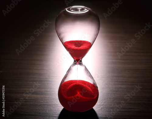 Crystal hourglass with red sand on dark background