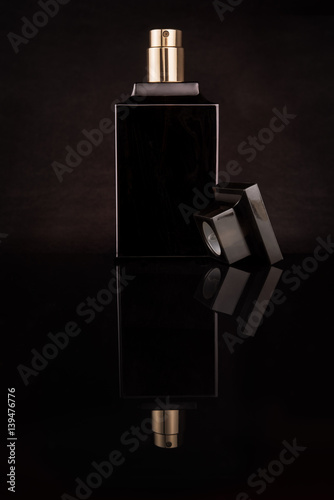 Dark, glass, elegeance bottle of perfume on a black background with mirror reflection made in photo studio.