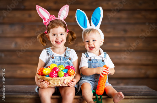 Photography Happy kids boy and girl dressed as Easter bunnies with basket of eggs on  wooden