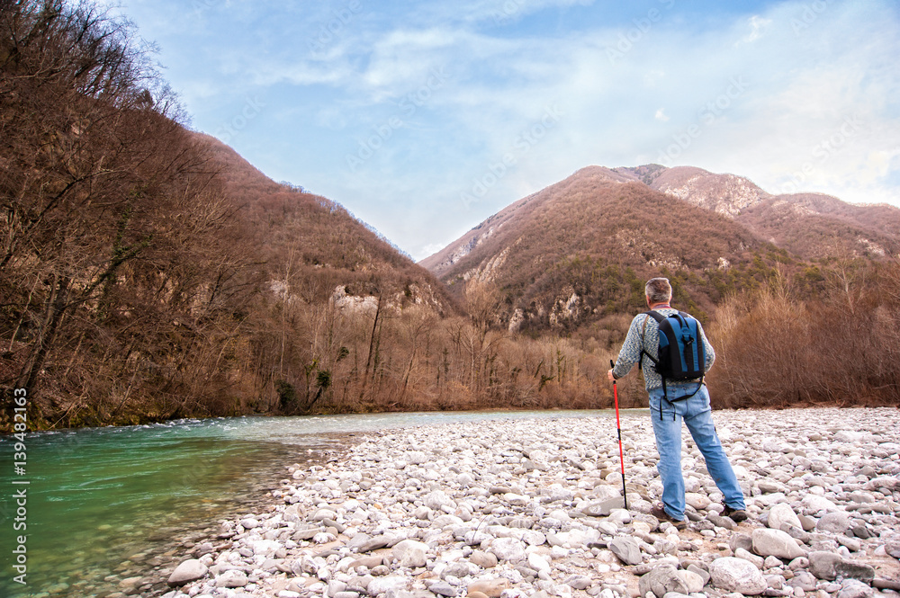 Hiker on the bank of a river. Walking toward mountain.