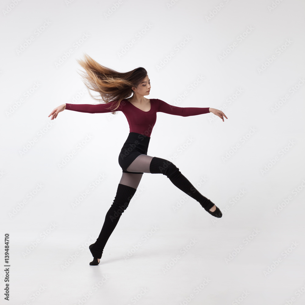 young beautiful woman dancer with long brown hair wearing maroon swimsuit posing on a light grey studio background