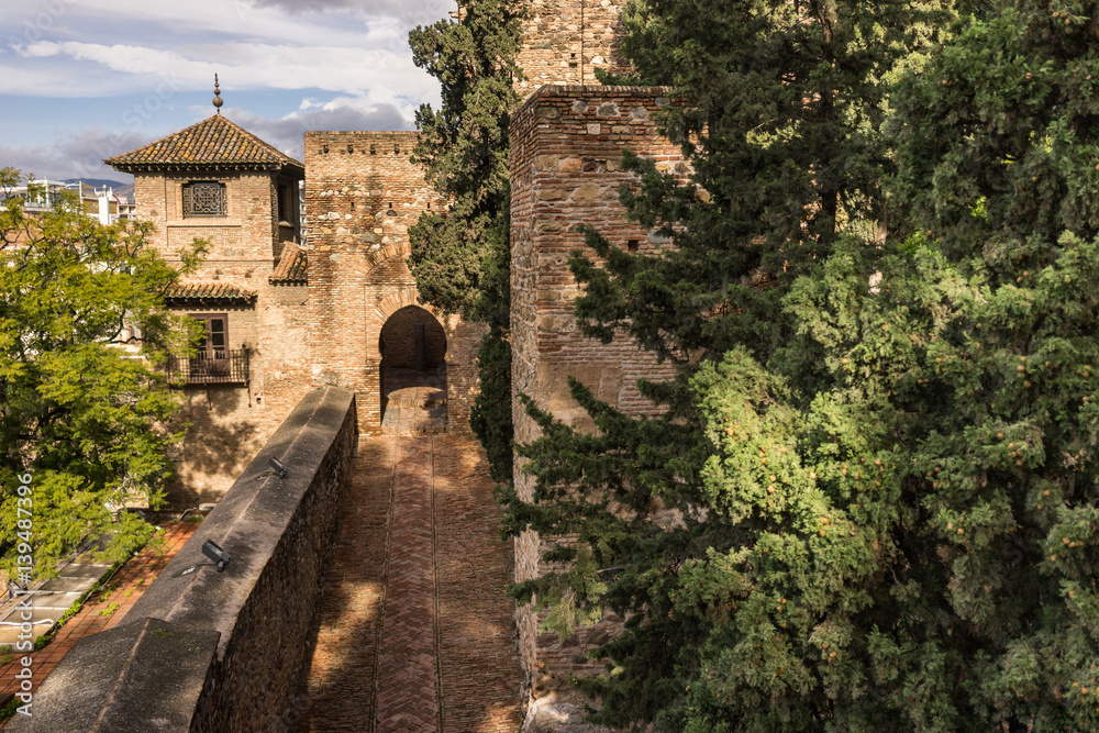 Medieval stone arches and walkway by the walls and towers of an ancient Alcazaba fortress in Malaga, Spain.