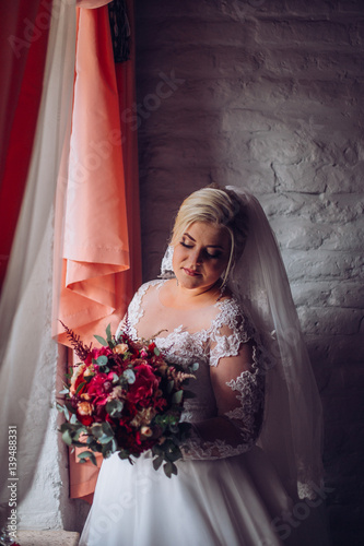 the bride in a wedding dress standing in a bright studio near the large windows