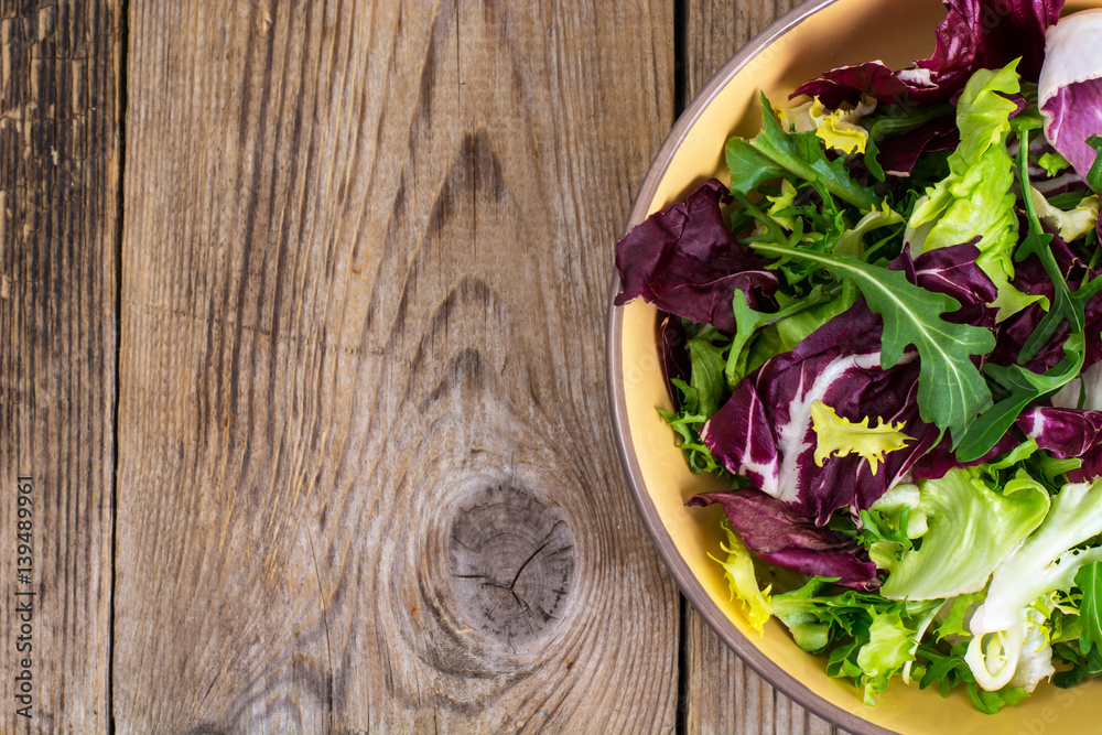 Frise, batavian, radichchio, arugula in a ceramic bowl on a wood