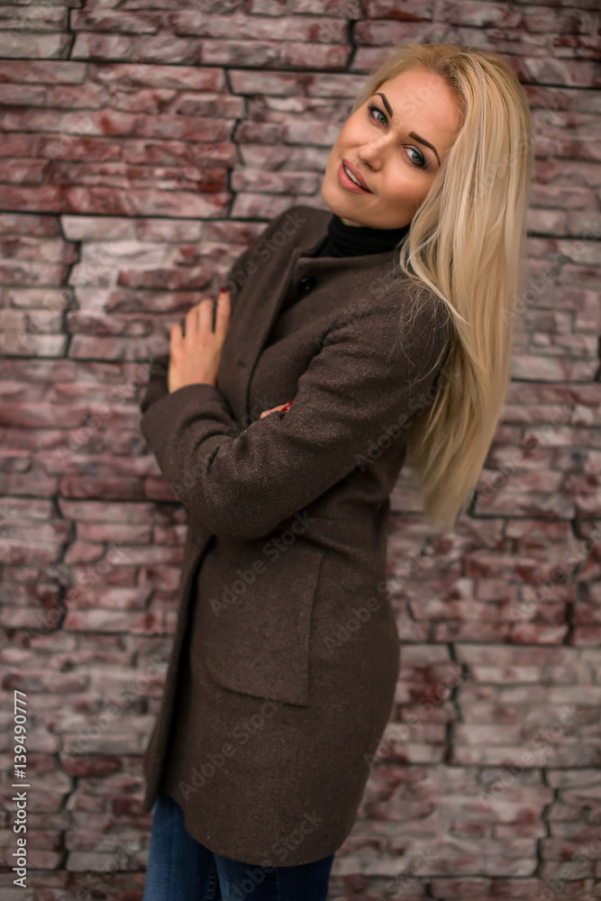 beautiful girl standing on the street in a coat near the tiles on the wall background autumn