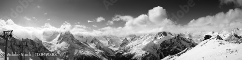 Black and white panoramic view on ski slope and cloudy mountains at sun day