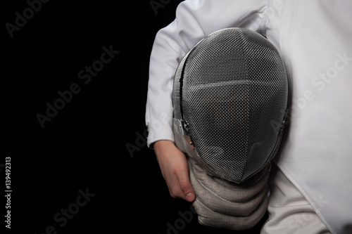 Fencer woman hold her helmet in hand wearing white fencing costume. Isolated on black background.