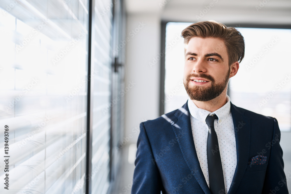 Young successful businessman standing in office looking out the window Young successful businessman standing in office looking out the window