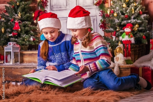 Girls children read a book near the Christmas tree.