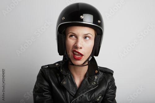 Portrait of biker woman over white background, female with funny face wearing stylish black sportive helmet and leather jacket. © face_reader_img