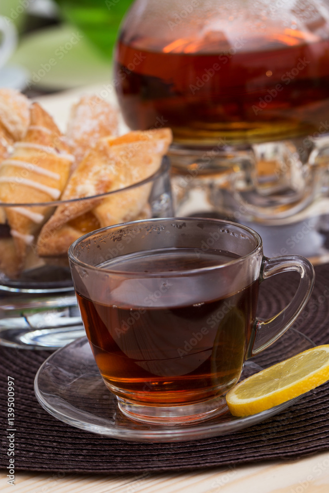 A pot of tea on the heater, and a cup of tea with lemon on a brown cushion table with cakes A pot of tea on the heater, and a cup of tea with lemon on a brown cushion table with cakes